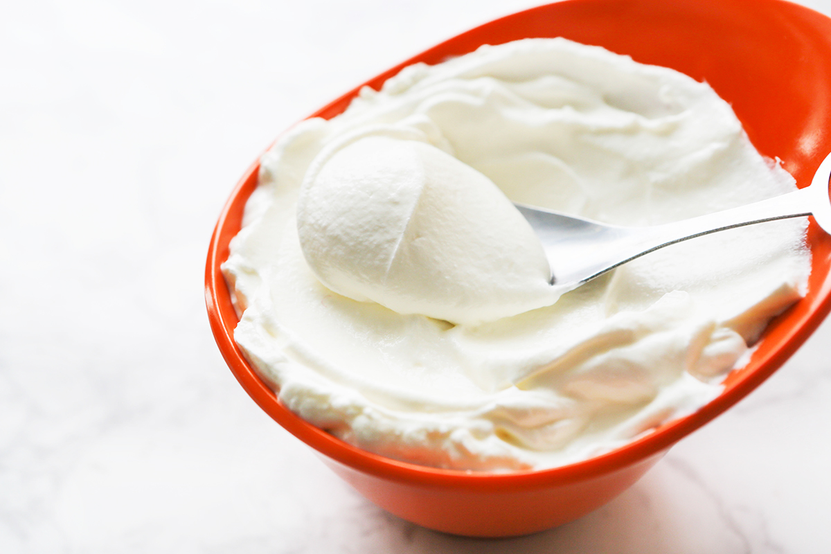 Orange bowl filled with creamy sour cream with a spoon inside.