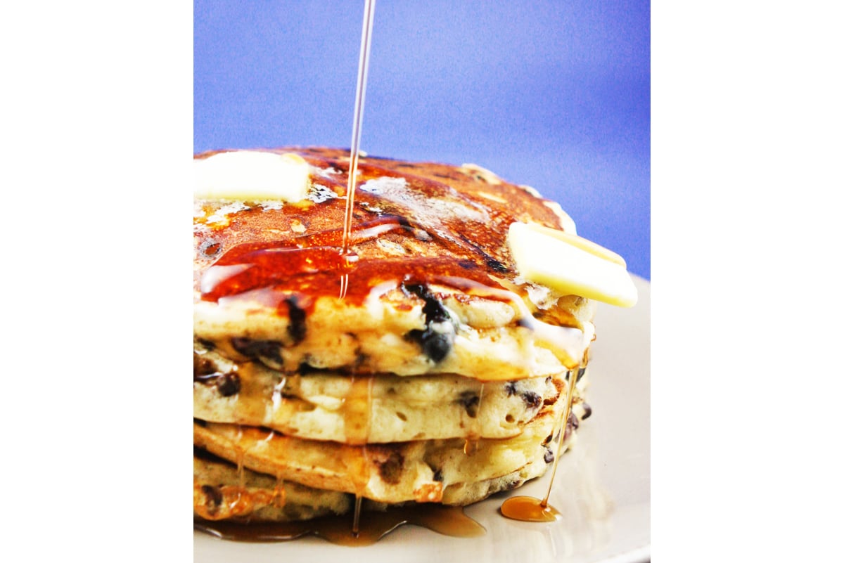 Syrup being drizzled over a tall stack of pancakes.