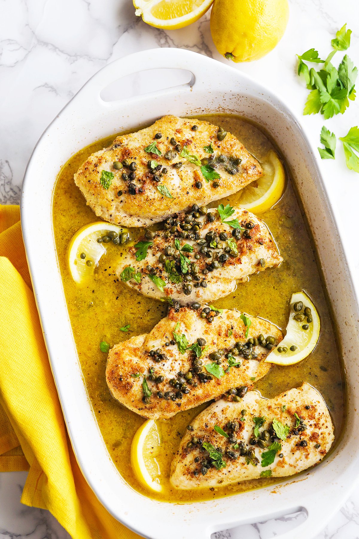 top view of baking dish filled with lemon chicken piccata surrounded by lemons.