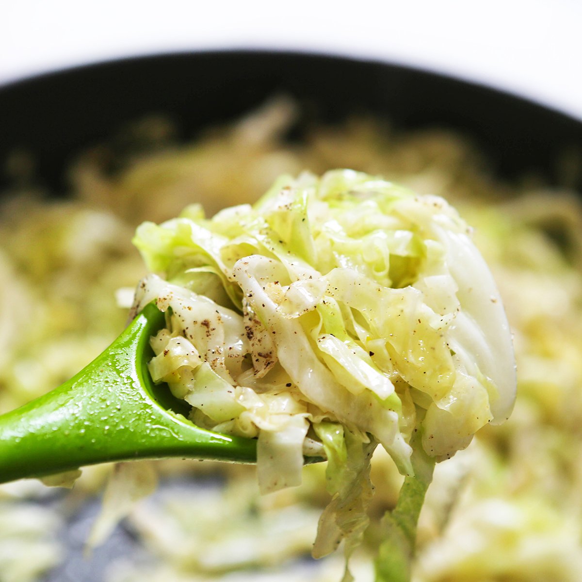 Spoon of sauteed cabbage being pulled from pan.