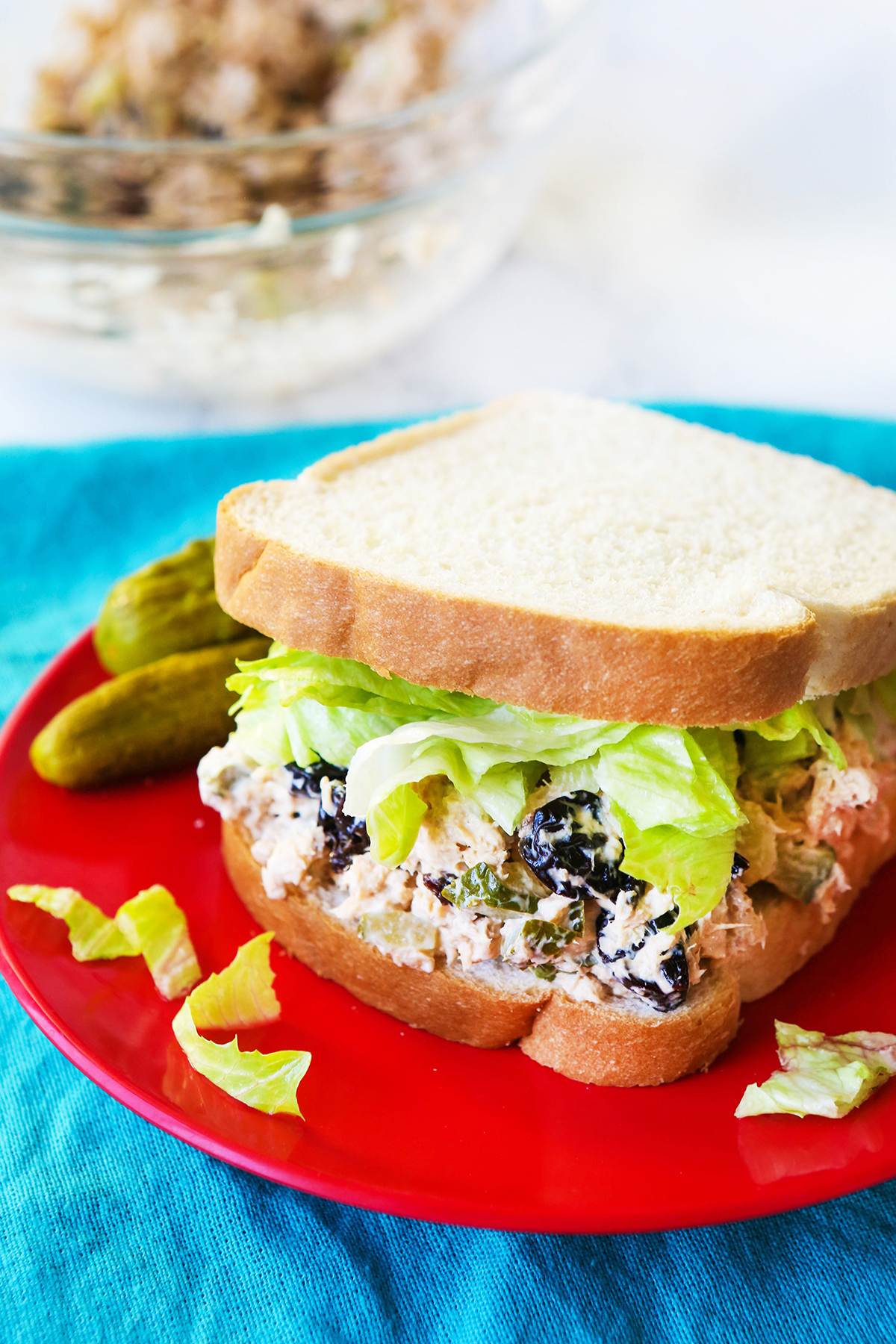 Chicken salad sandwich on a red plate with dill pickles sitting by it.