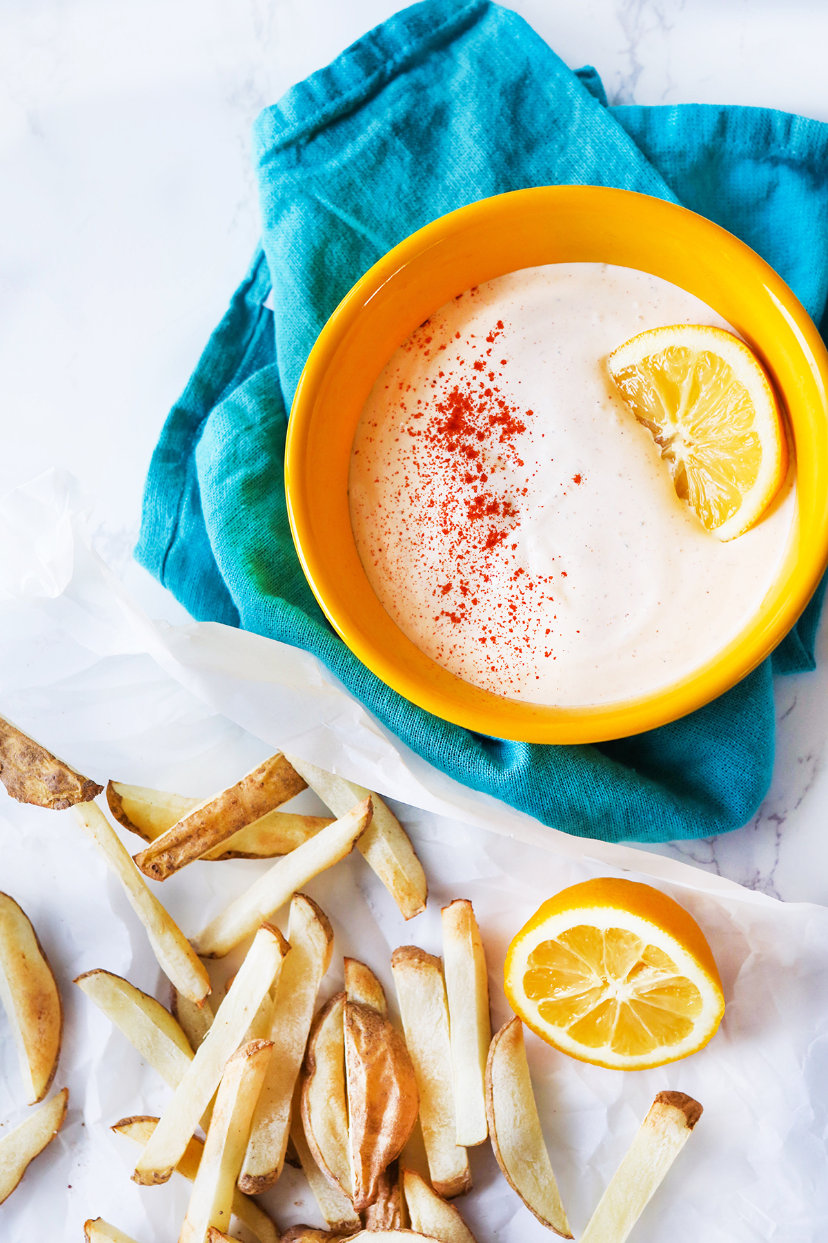 Bowl of seasoned sour cream sitting next to a pile of french fries.