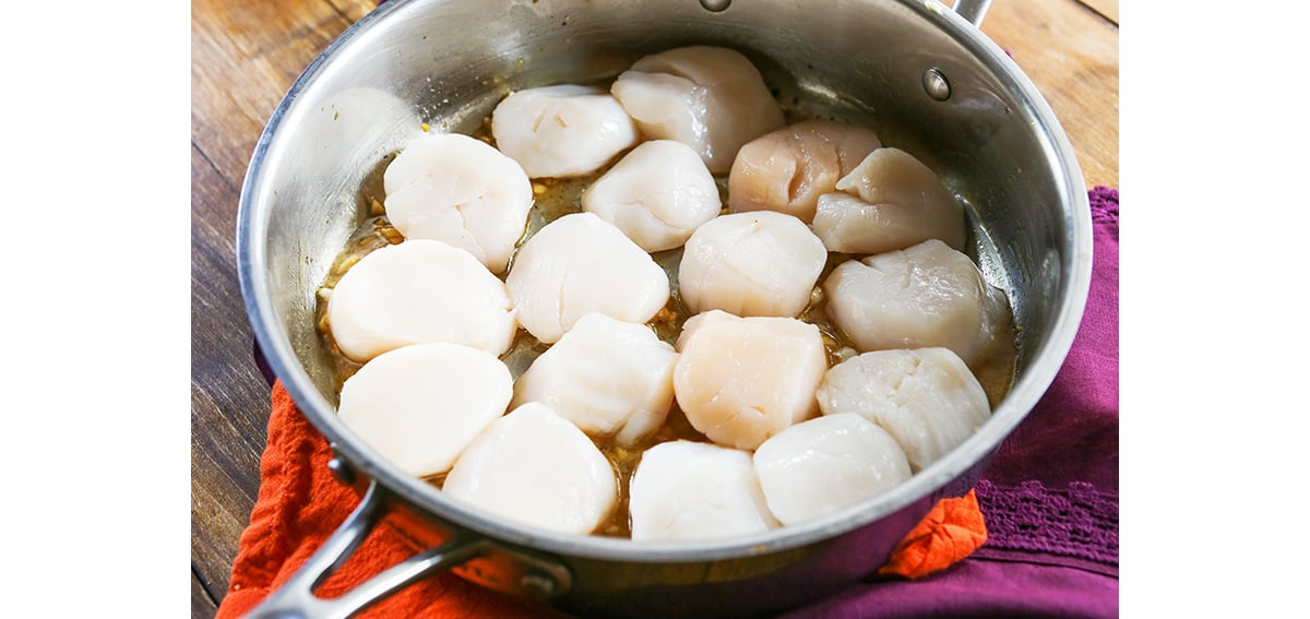 Fresh scallops lined up in a single layer in a skillet.