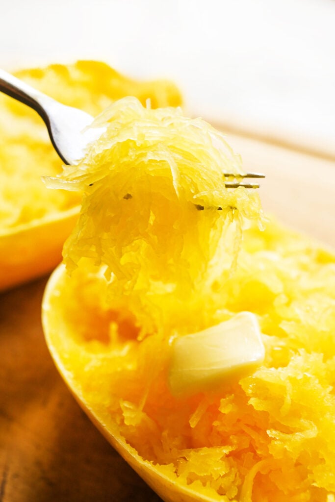 Spaghetti squash with a pat of butter melting and a fork pulling a bite out.