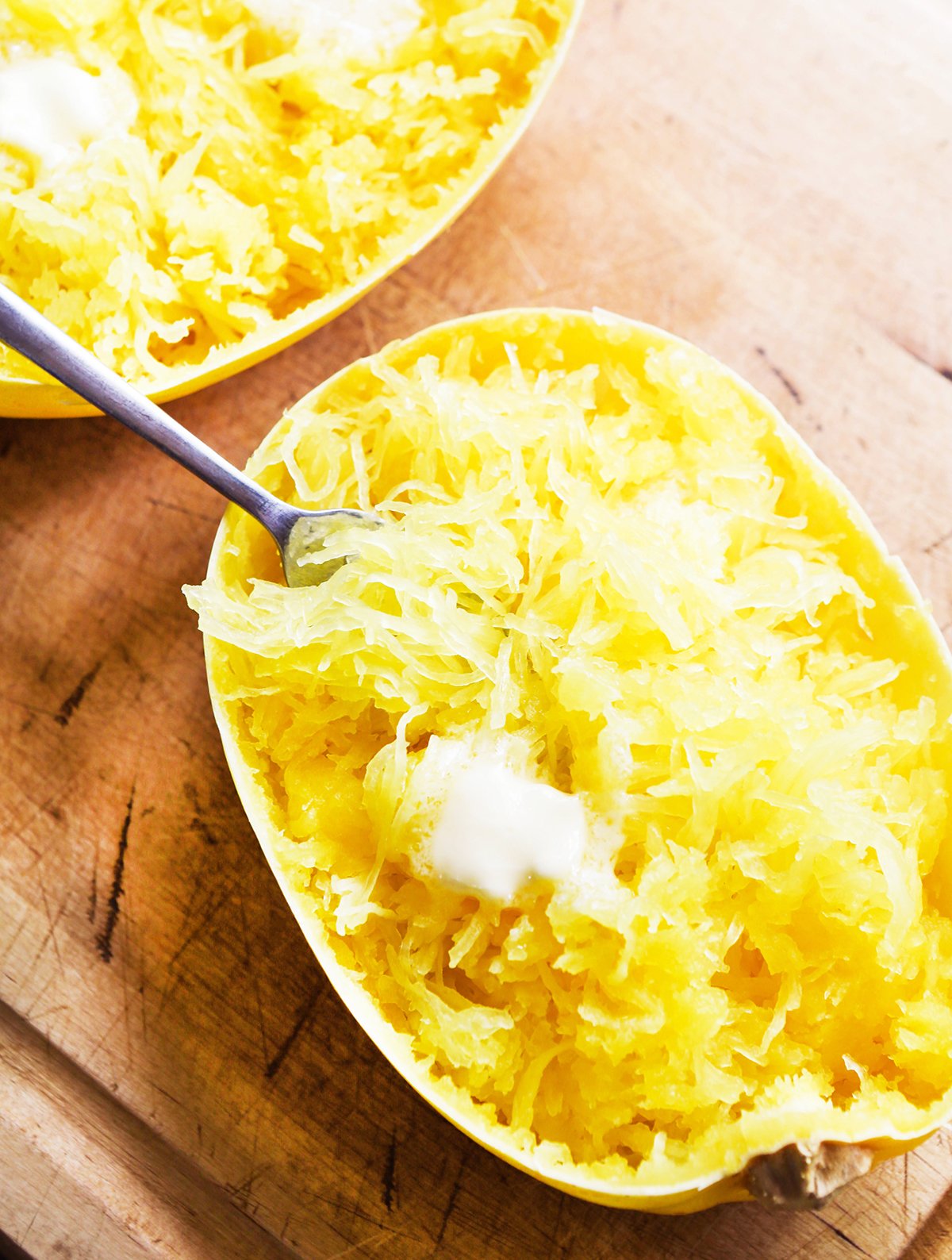 top view of a half spaghetti squash with a fork in it with melting butter on top.