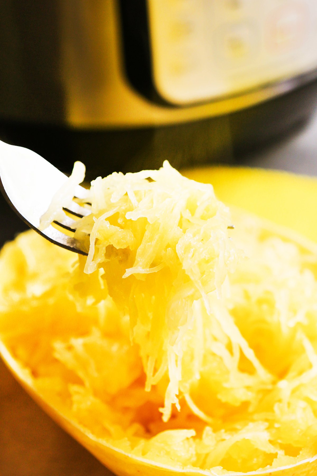Fork tines filled with cooked spaghetti squash in front of an instant pot.