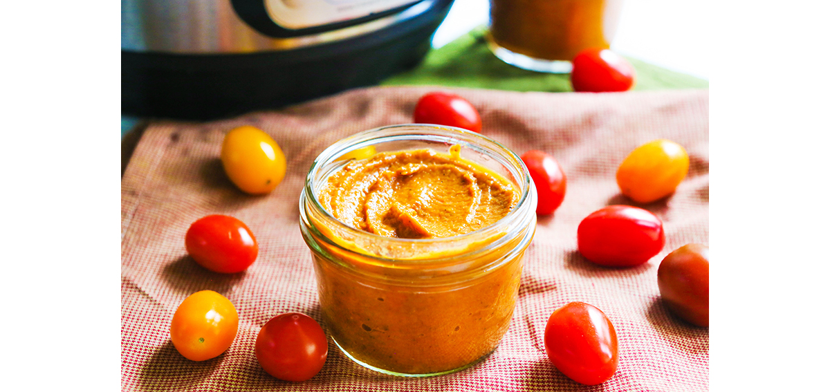 Small mason jar filled with tomato sauce and surrounded by cherry tomatoes.