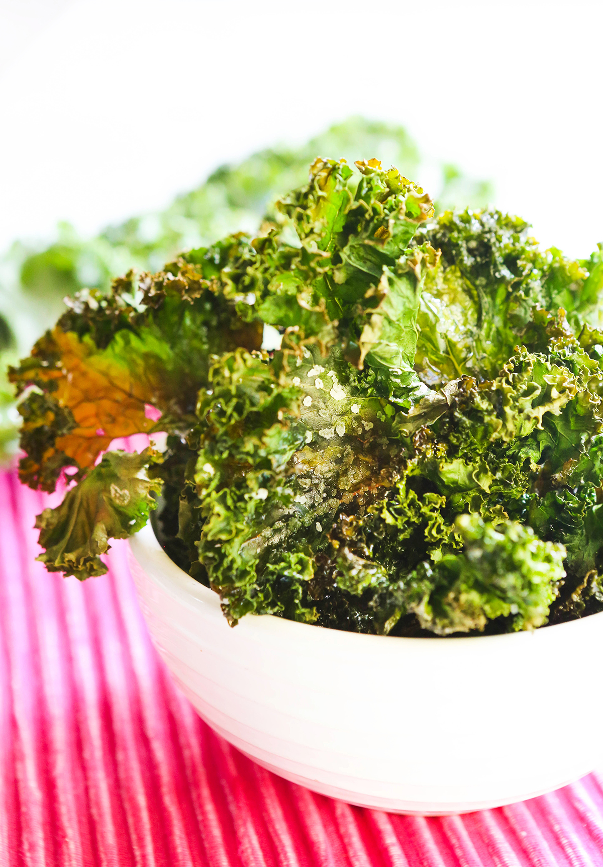 Bowl full of crispy kale with fresh uncooked kale on the side.