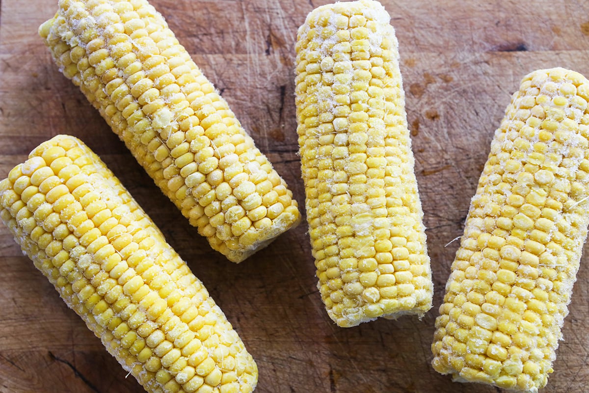 Four frozen ears of corn on a cutting board.