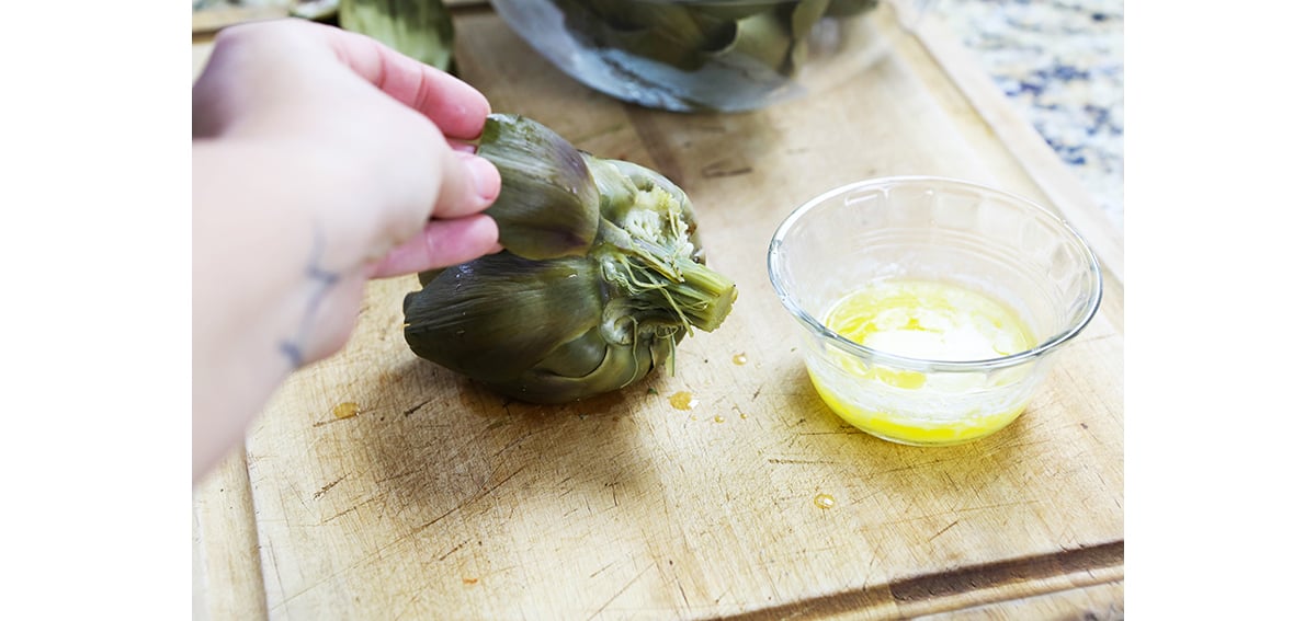 Fingers pulling artichokes leaves off the vegetable.