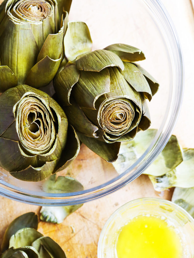 Steamed artichokes in a serving bowl sitting next to a small bowl of melted butter.
