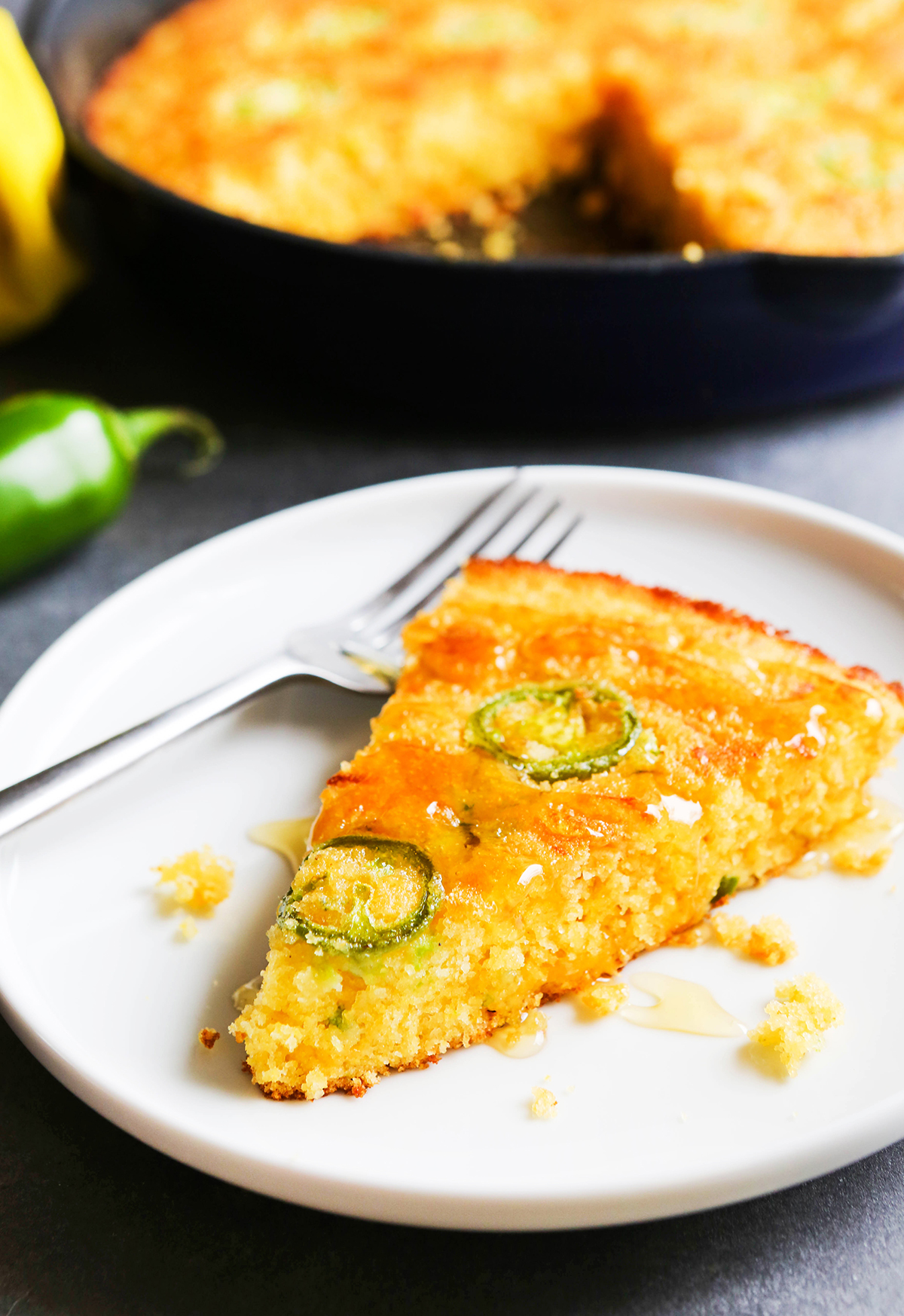 Slice of cornbread on a plate, sitting next to a cast iron pan.