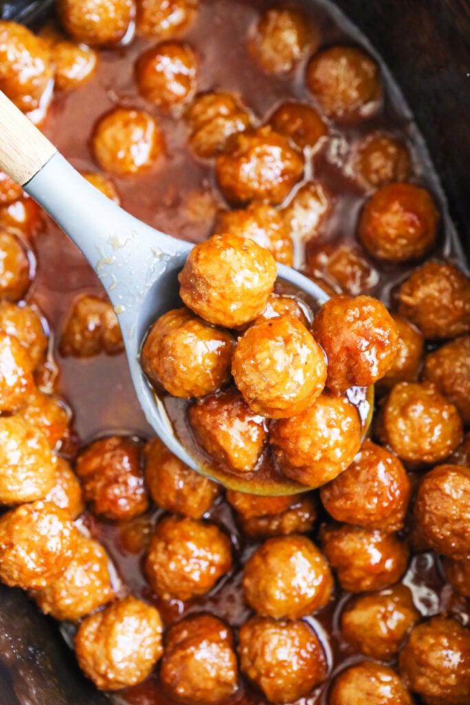 Spoonful of party meatballs hovering over a crockpot.