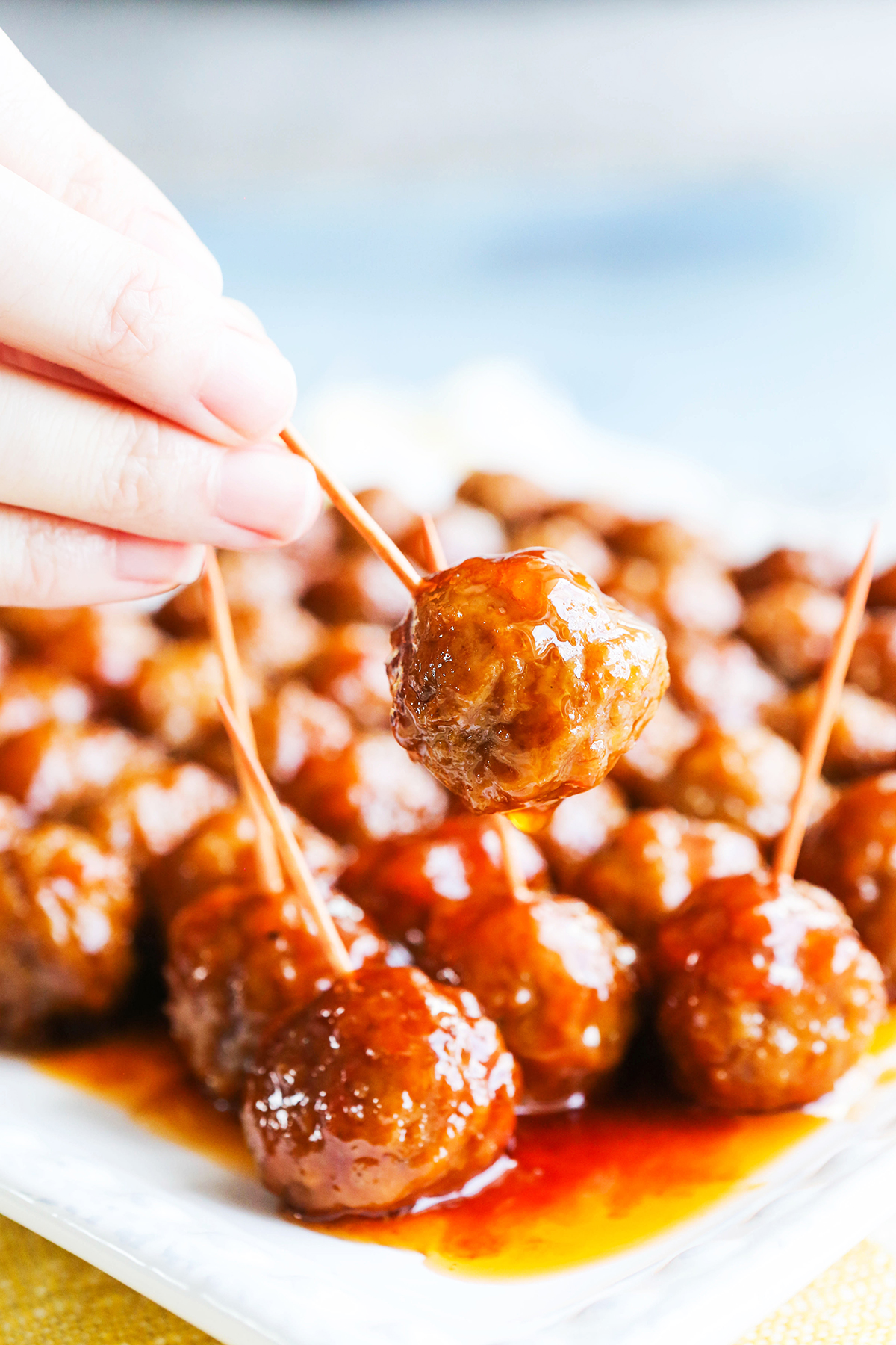 Hand pulling a meatball off a serving plate with a toothpick.