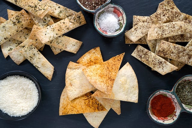 Versions of crispy baked tortilla chips with seasonings in containers next to the chips. 