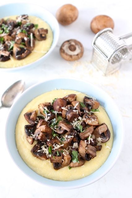 Bowl of polenta with roasted mushrooms on top with a spoon next to it. 