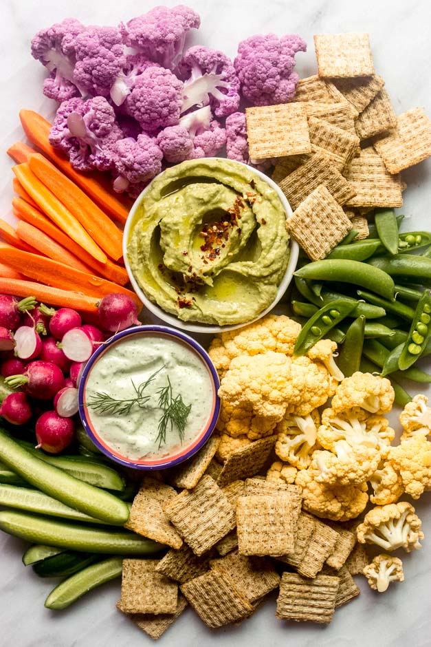 Colorful vegetables with two green dips displayed in the middle on a platter. 