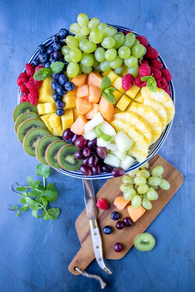 Fruit platter with arranged colorful fruit pieces next to a cutting board. 