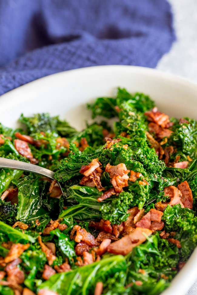 Sauteed bacon and kale with a serving spoon tucked in. 