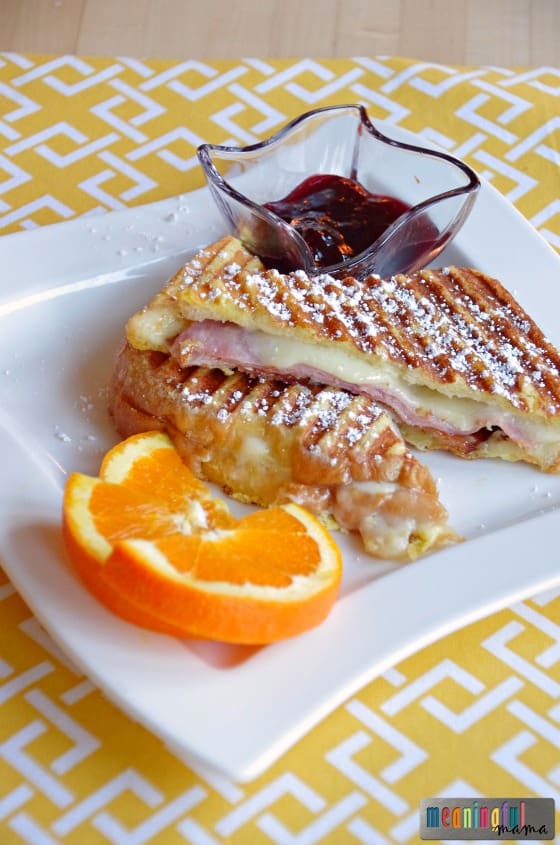 Monte Cristo sandwich cut in half and on a plate with an orange garnish. 