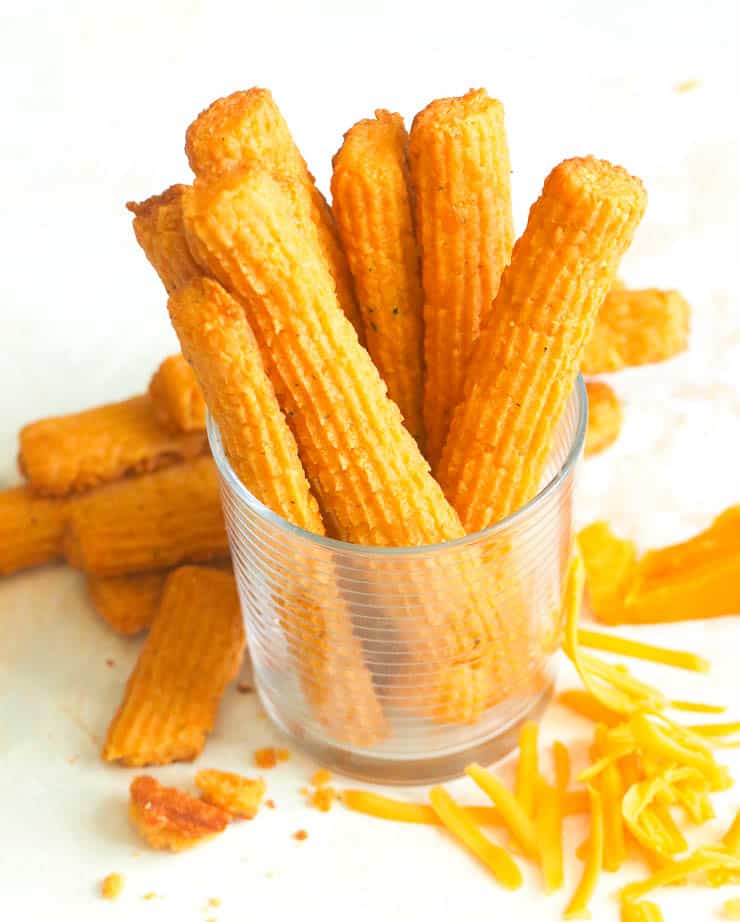 Cheese straws in a glass jar with cheese shavings next to it. 