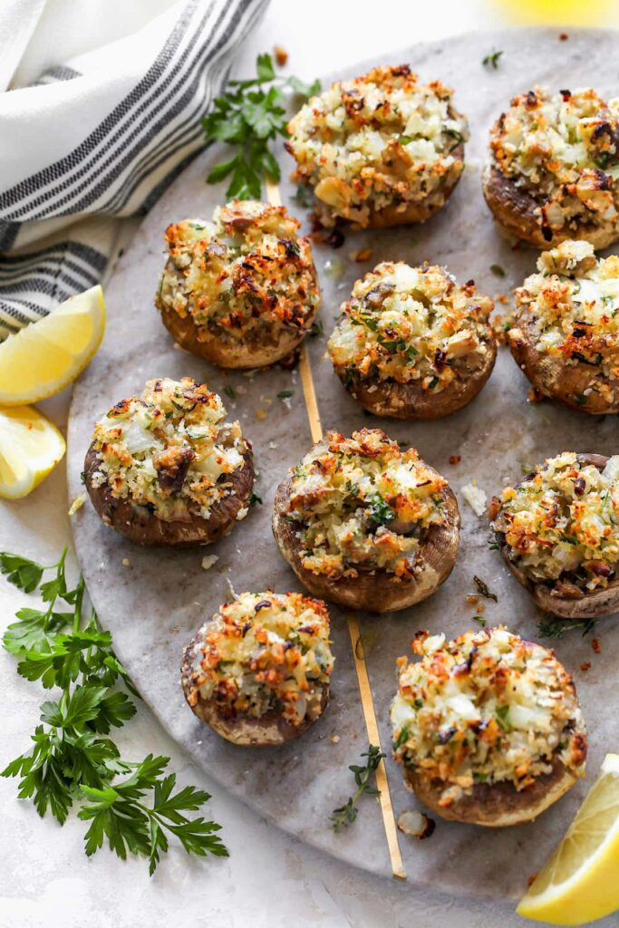 Stuffed mushrooms sitting on a platter with lemon slices. 