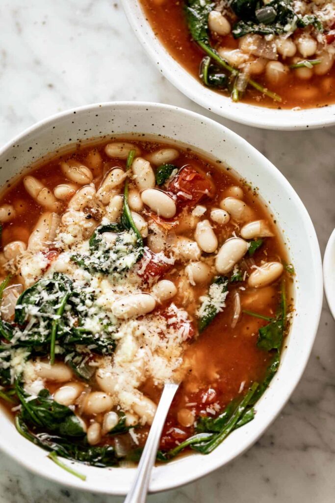 Bowl of white bean soup topped with shredded parmesan. 