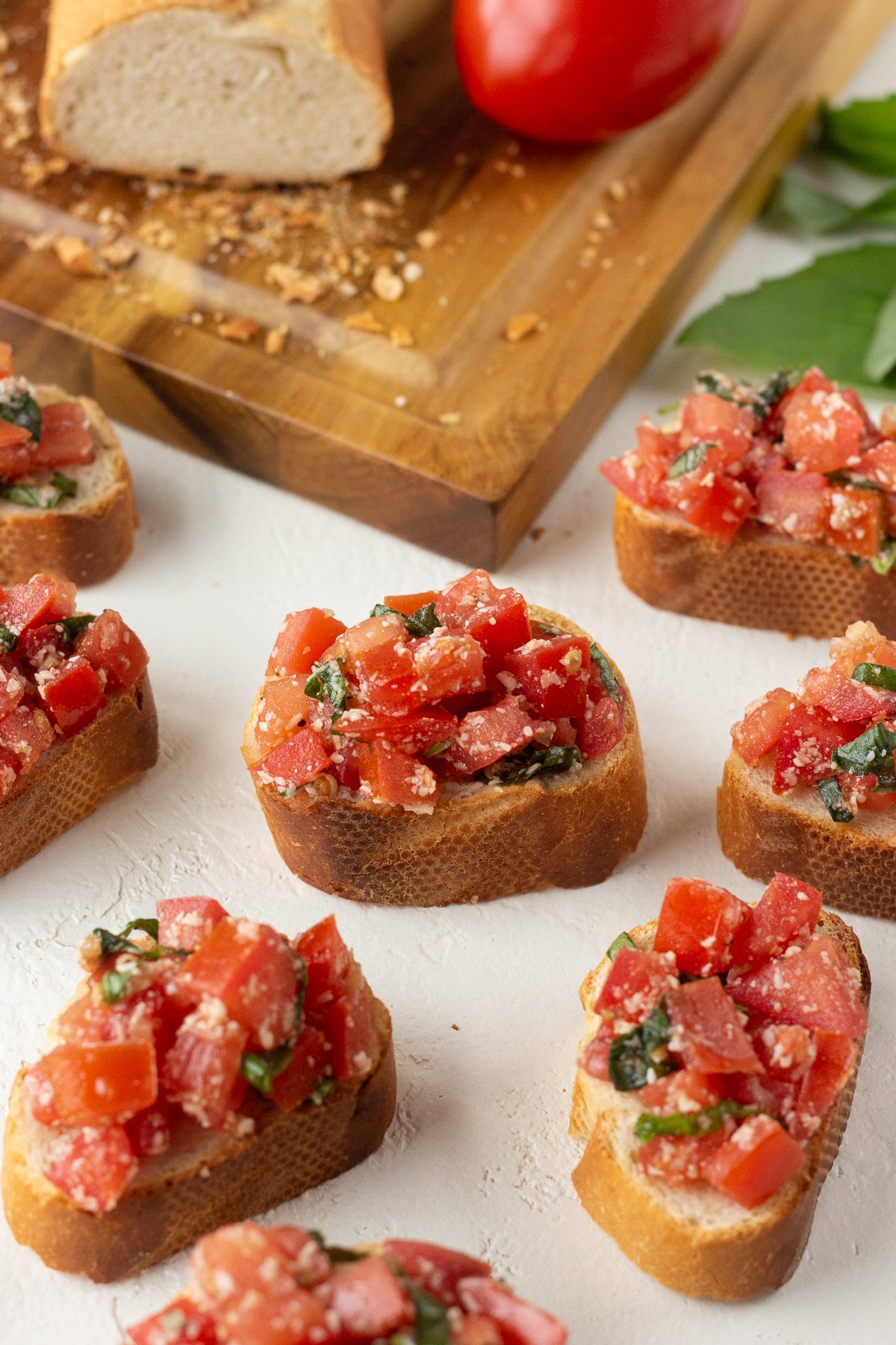 Tomato mixture on top of pieces of French bread slices, sitting next to a cutting board.