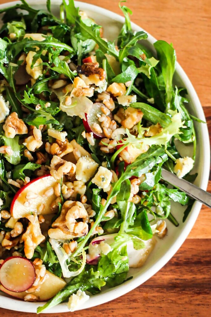 Serving bowl of blue cheese, apple, grape and walnut salad with a spoon. 