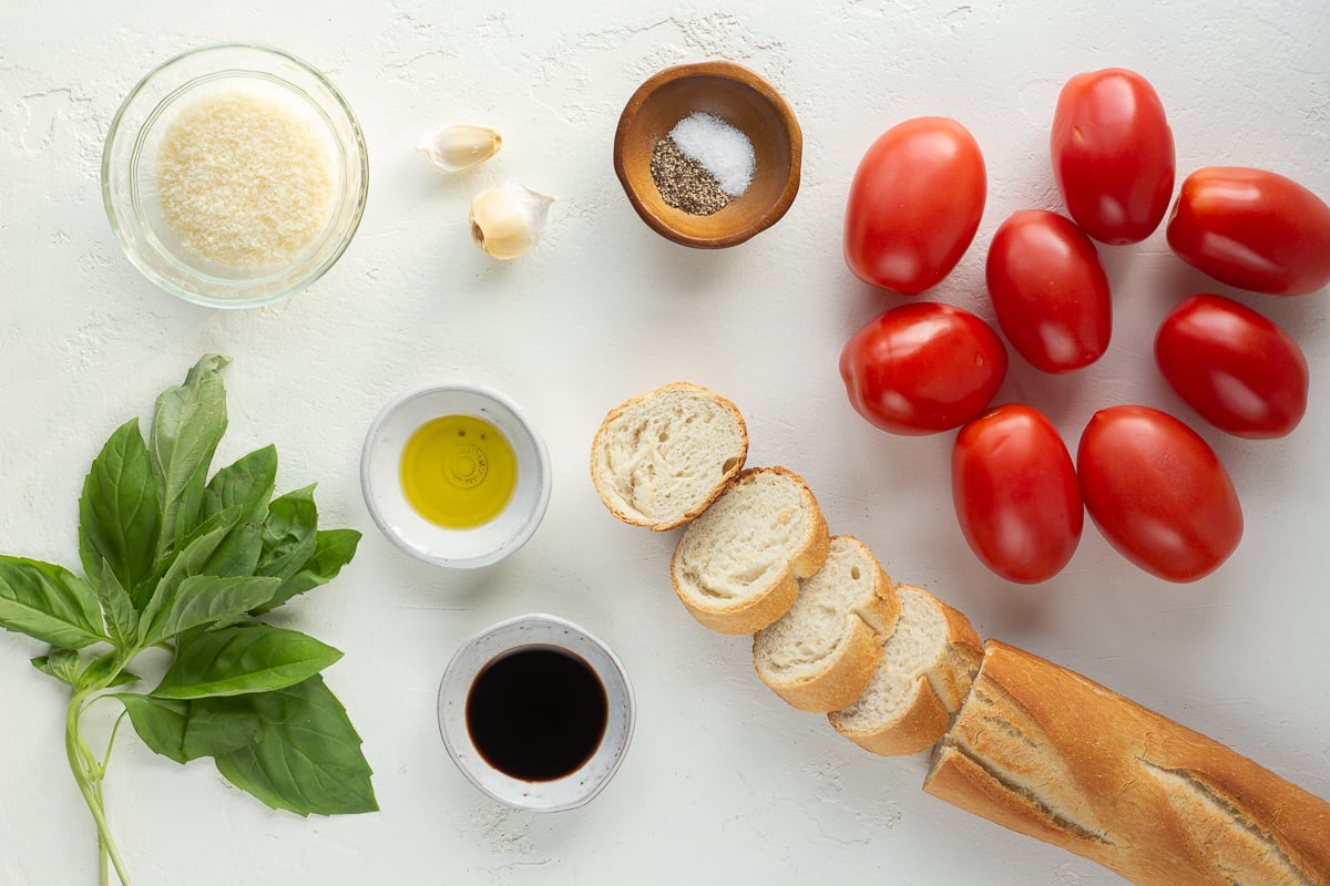 Tomatoes, French bread, basil and other ingredients on a white backdrop meant for making bruschetta.