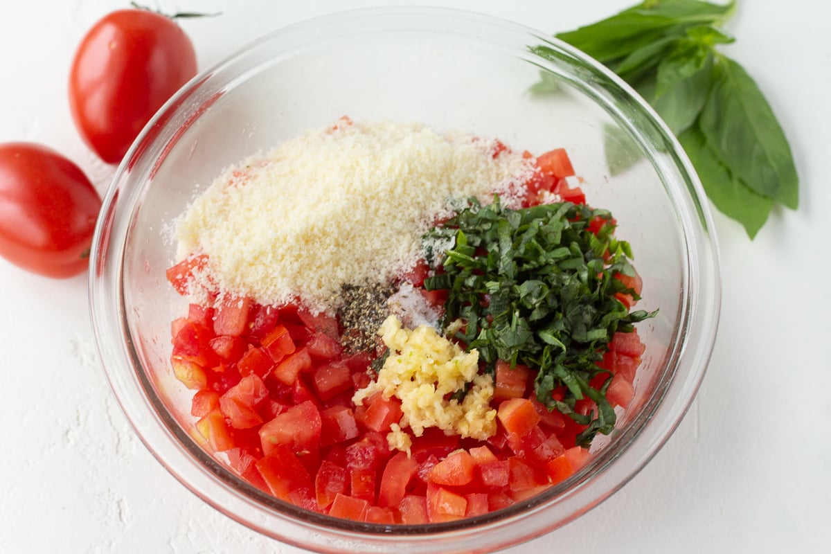 Mixing bowl filled with chopped tomatoes, basil and parmesan cheese.