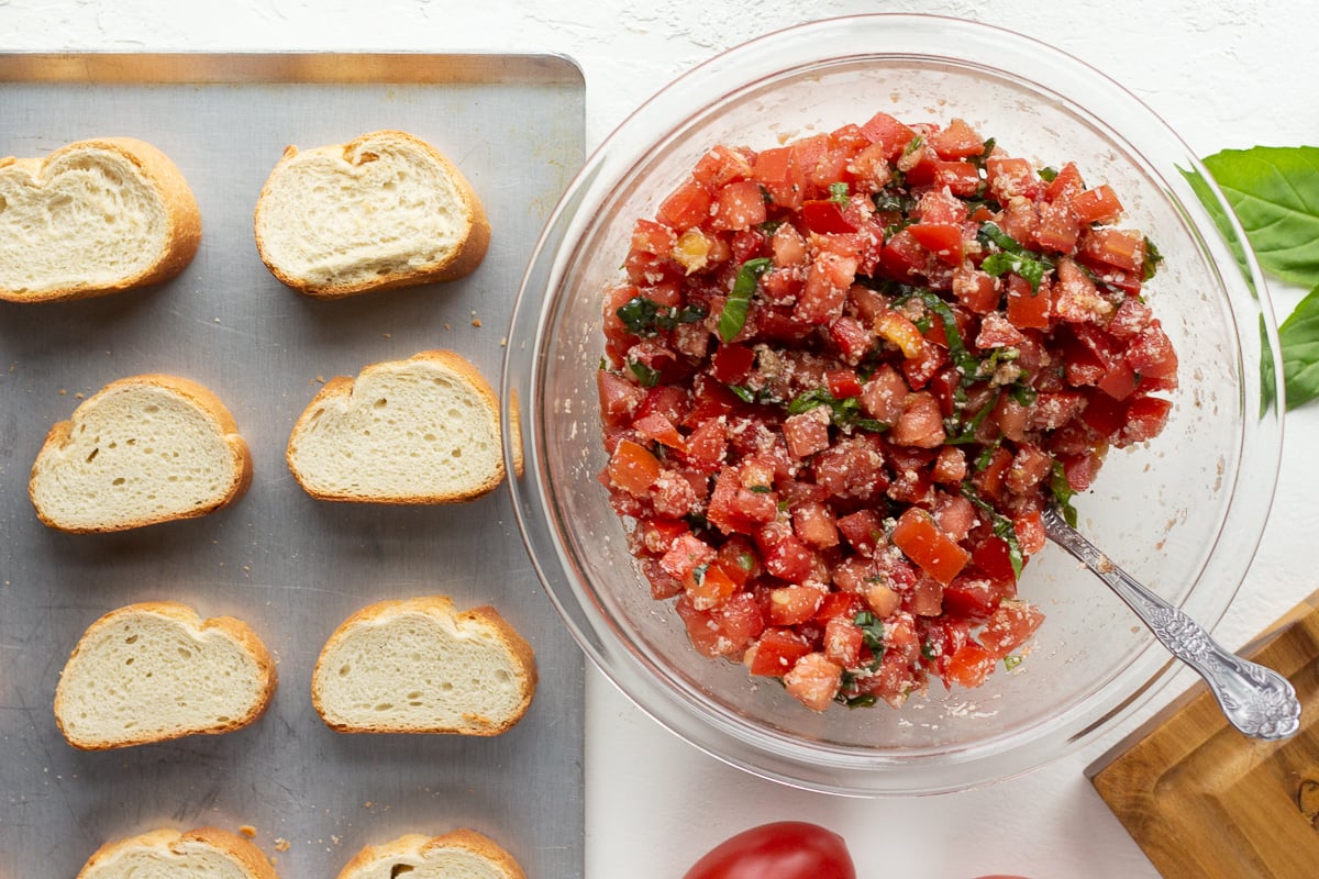 Tomato spread mixture in a bowl, sitting next to a baking sheet lined with french bread slices.