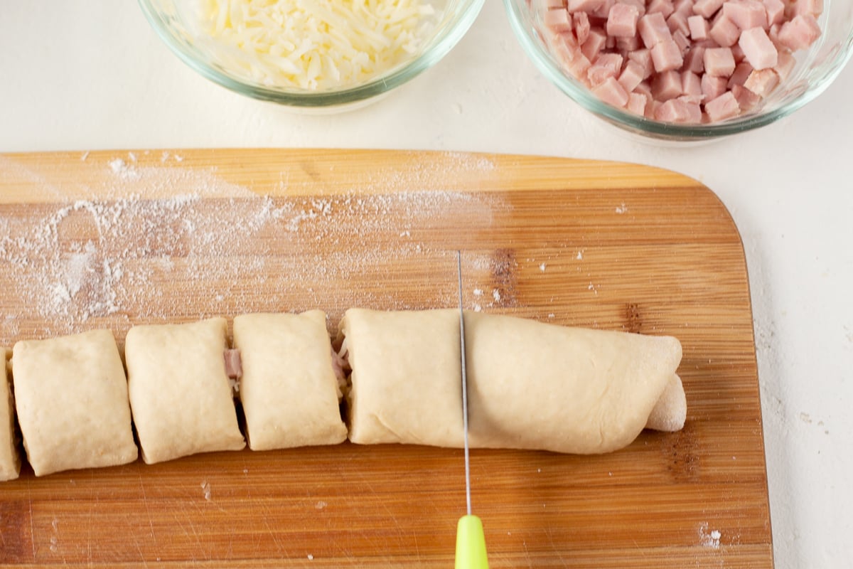 Roll of dough being cut into equal pieces on a cutting board.