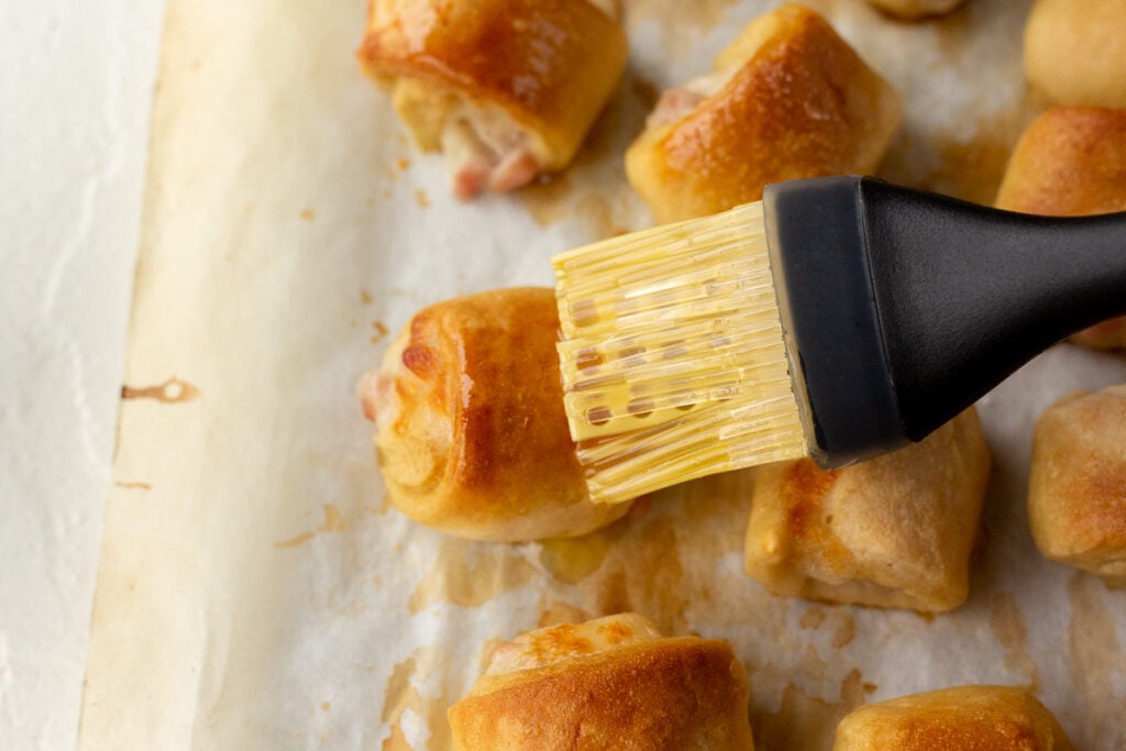 Pretzel bites being brushed with a buttery pastry brush.