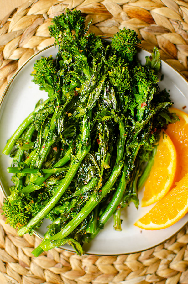 Roasted broccoli rabe on a plate with orange slice garnishes. 