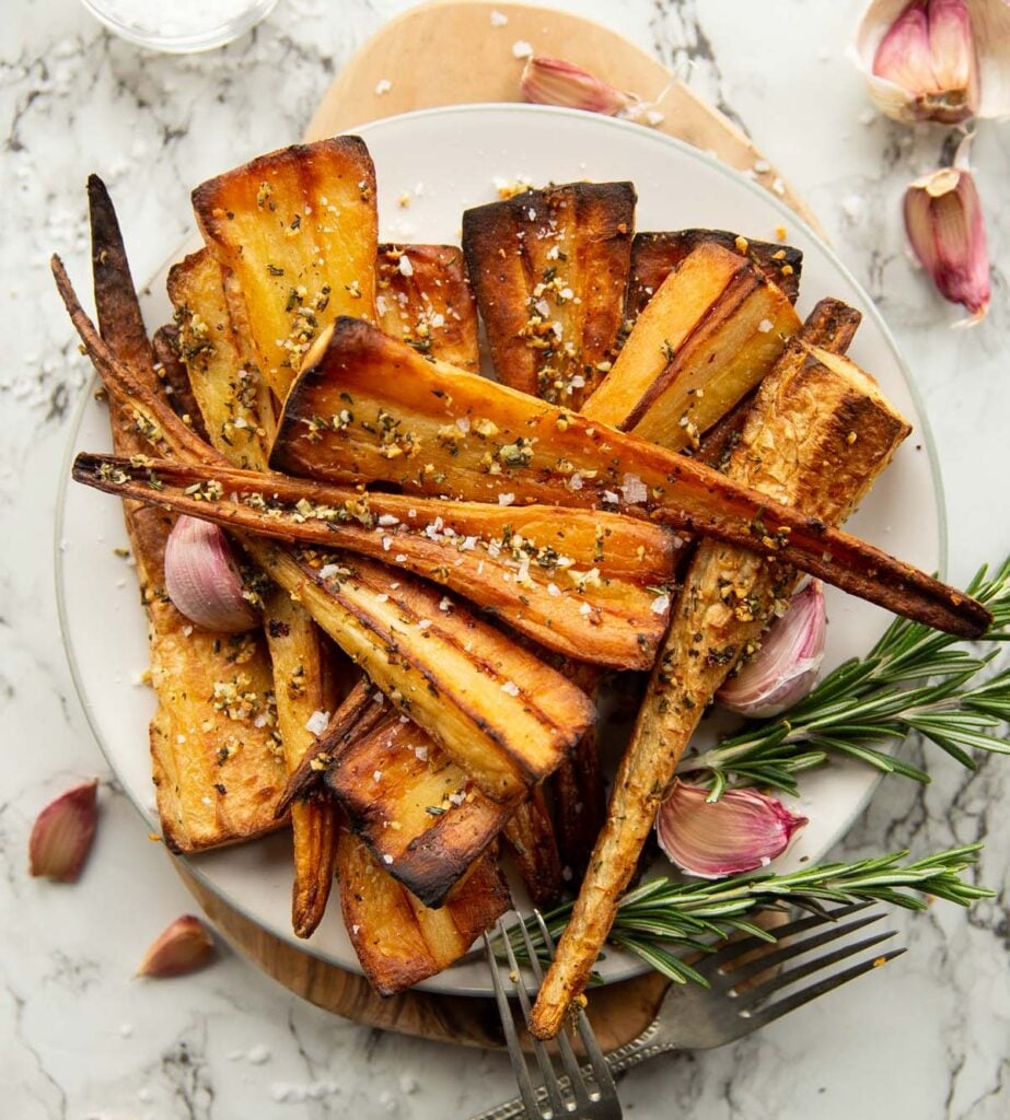 Roasted parsnips on a plate with rosemary sprigs and garlic cloves on the side.
