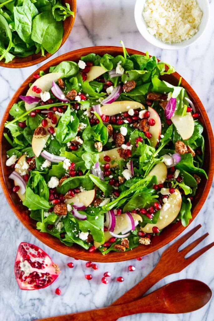 Bowl of spinach pomegranate salad with a small bowl of feta cheese next to it. 