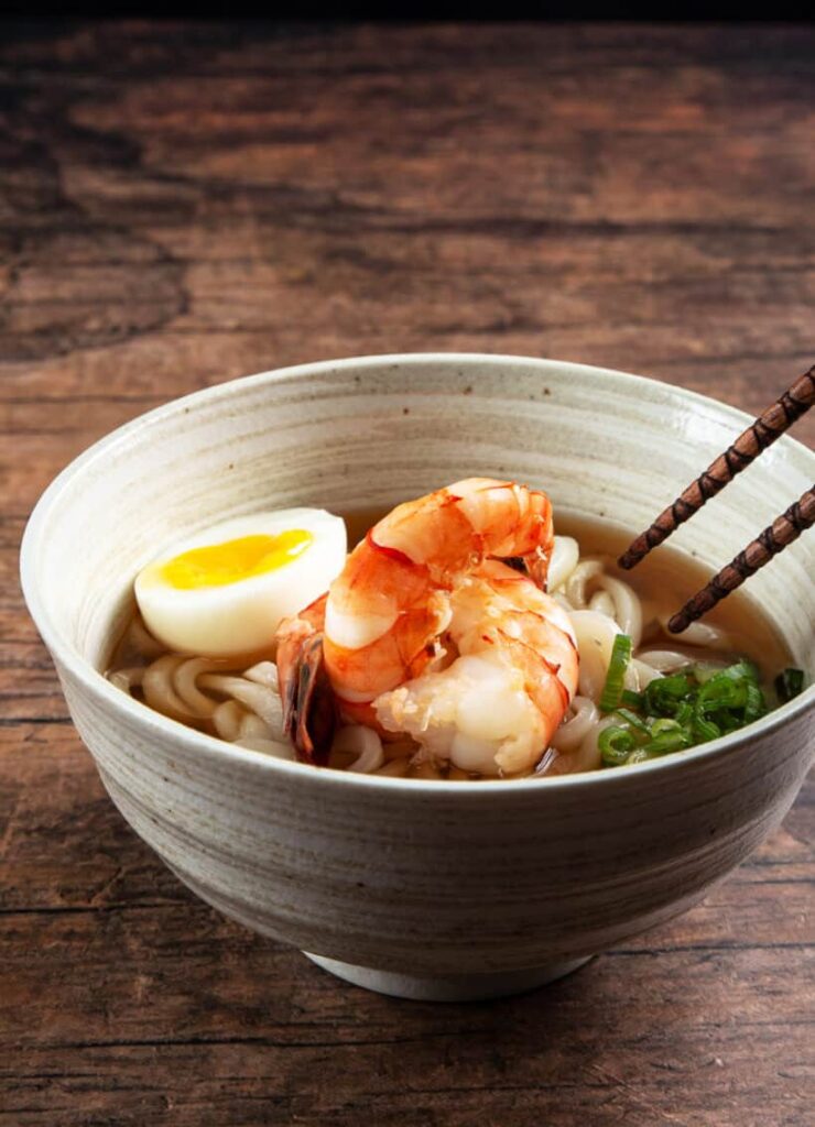 A set of chopsticks inside a bowl of udon soup. 