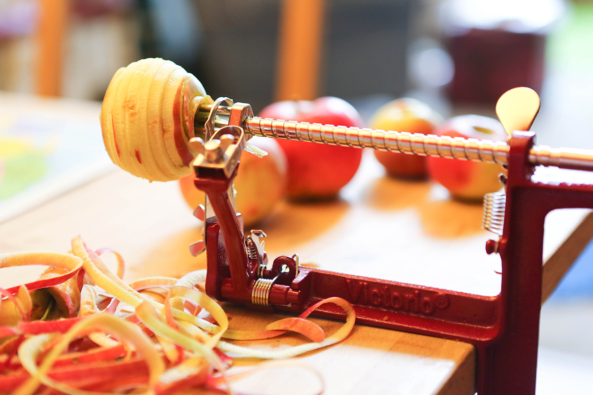 An apple stuck into the end of an apple peeler and corer secured to the edge of a table.