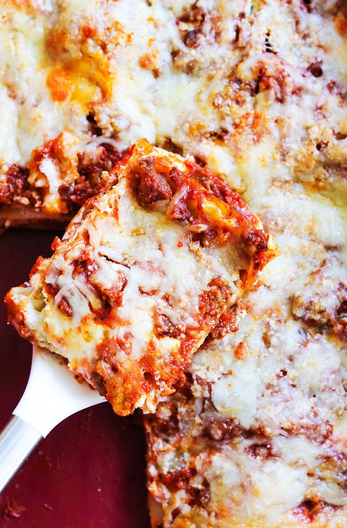Slice of lasagna on a spatula, resting inside a pan of lasagna.
