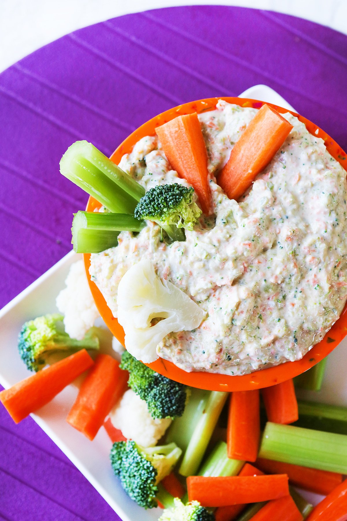 Veggie sticks packed into an orange bowl filled with creamy vegetable dip.