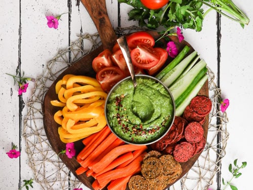 Spicy Herb Avocado dip on a charcuterie board surrounded by sliced veggies and chips. 