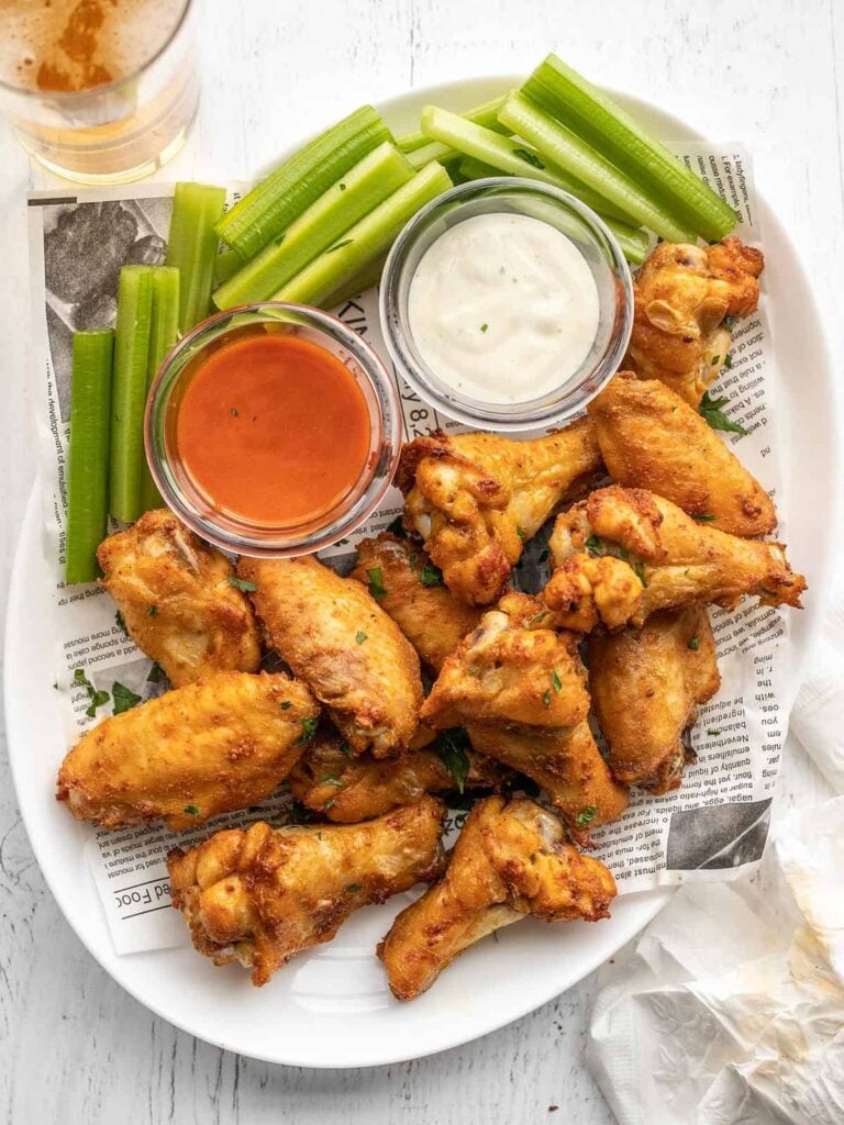 Baked chicken wings on a serving platter along with celery and dip. 