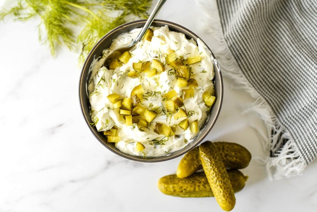 Top view of pickle dip with dill pickles sitting next to it. 