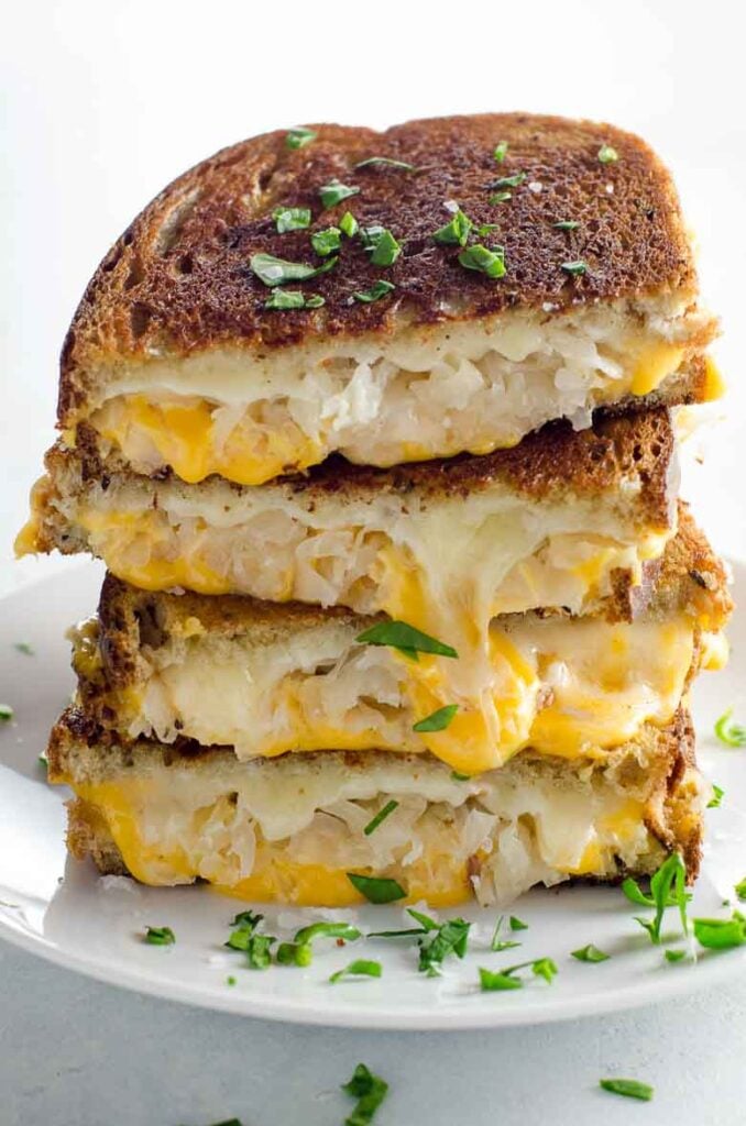 Grilled cheese with sauerkraut and dijon cut in half and stacked on a plate. 