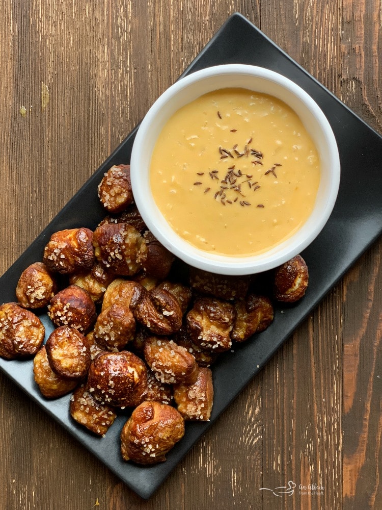 Pretzel bites with sauerkraut cheddar cheese sauce on a serving tray. 