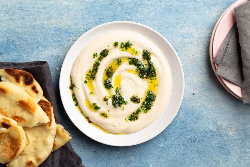 Garlic white bean dip with olive oil and pesto drizzled on top next to naan bread. 