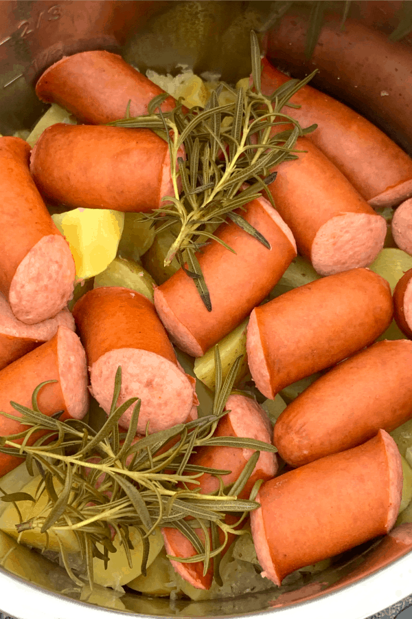 Potatoes, sausage and sauerkraut cooked inside an Instant Pot with fresh rosemary sprigs on top. 