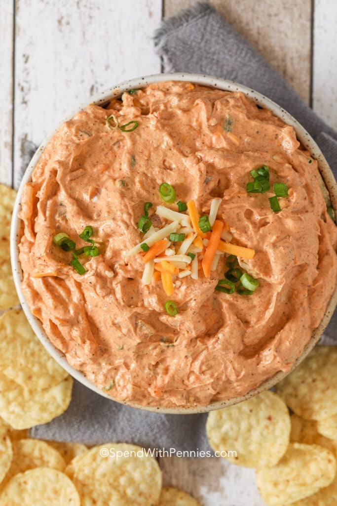Top view of a bowl of cream cheese dip garnished with shredded cheese and green onions. 