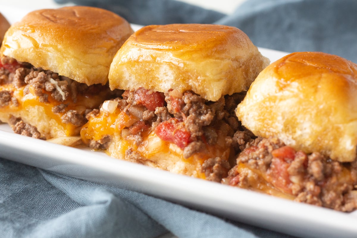 Cheesy ground beef sliders lined up on a serving platter.